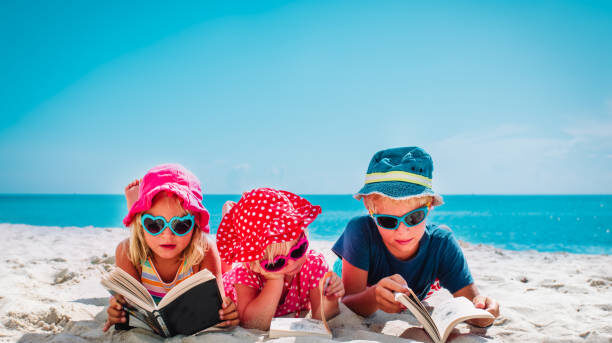 cute happy kids -boy and girls- read books on beach, family vacation concept