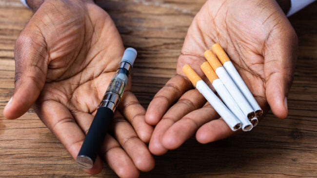 hands-holding-a-vape-pen-and-cigarettes