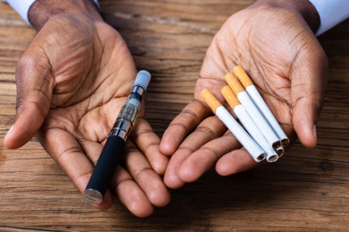 hands-holding-a-vape-pen-and-cigarettes